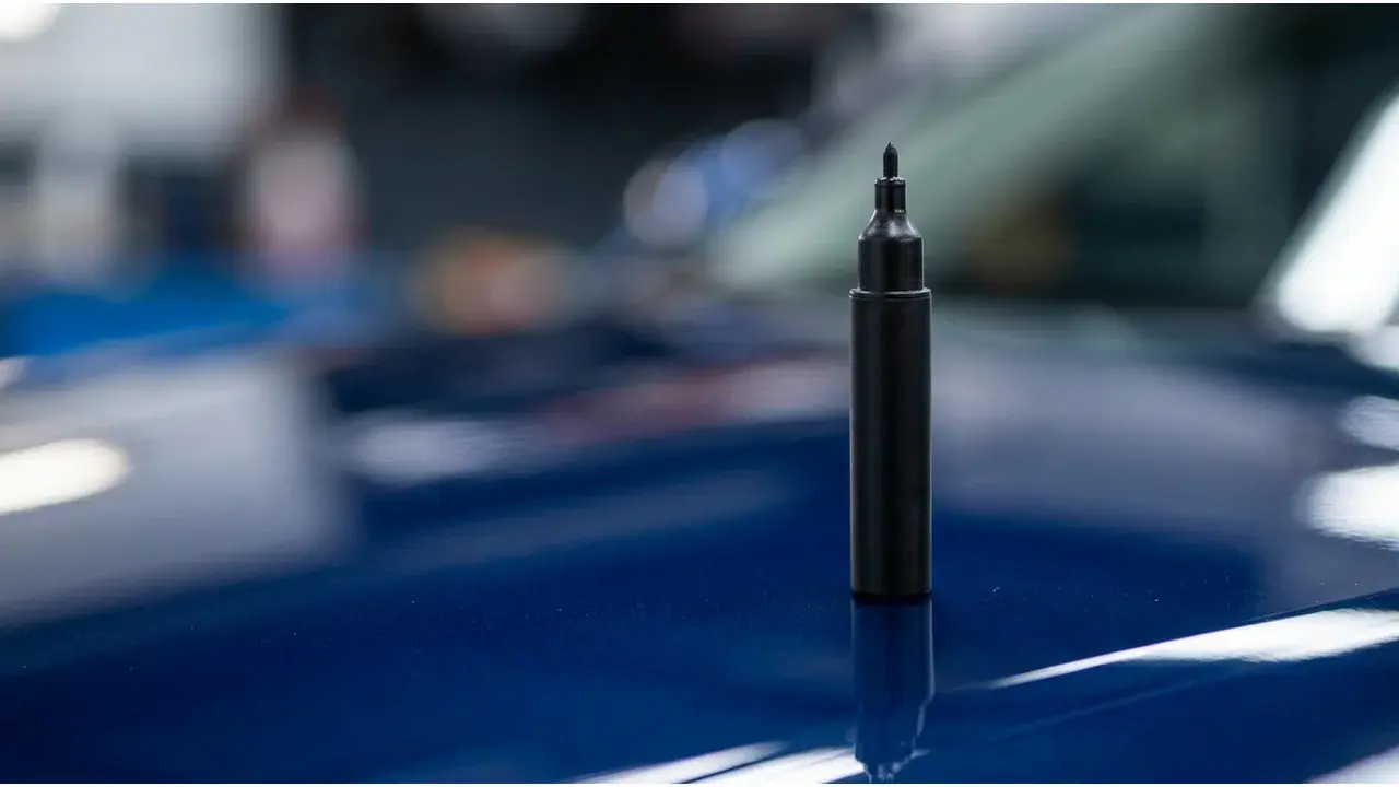 Stylo de retouche de peinture automobile à pointe fine posé sur une carrosserie bleue brillante